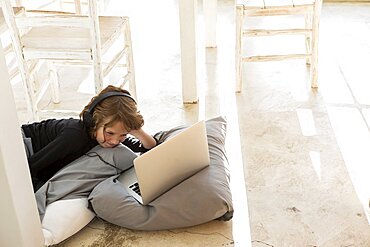 Eight year old boy lying on the floor on cushions using a laptop, Stanford, South Africa