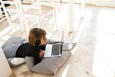 Eight year old boy lying on the floor on cushions using a laptop, Stanford, South Africa