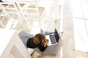 Eight year old boy lying on the floor on cushions using a laptop, Stanford, South Africa