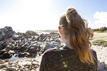 Teenage girl looking out over a beach and jagged rocks to the ocean, Pearly Beach, Gansbaai, Western Cape, South Africa