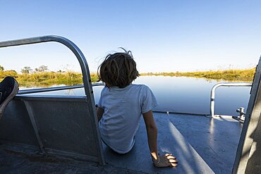 A boy on a motorboat travelling along a waterway in the Okavango delta, Okavango Delta, Botswana