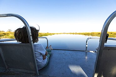 A boy on a motorboat travelling along a waterway in the Okavango delta, Okavango Delta, Botswana