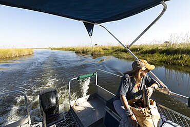 A woman with a water flask seated on a motorboat travelling along a waterway, Okavango Delta, Botswana