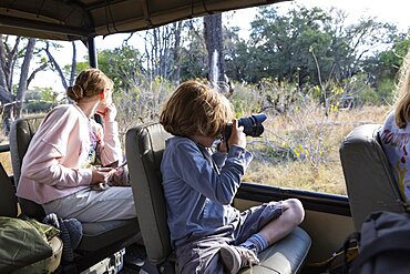 Young boy using a camera in a safari jeep, Okavango Delta, Botswana
