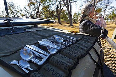 A meal stop on safari, people having drinks, and a roll of cutlery spread on the dashboard of a safari vehicle, Okavango Delta, Botswana