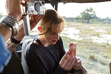 Teenage girl using smart phone to take a picture during a safari jeep drive, Okavango Delta, Botswana