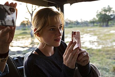 Teenage girl using smart phone to take a picture during a safari jeep drive, Okavango Delta, Botswana