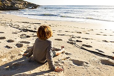 Young boy sitting on a sandy beach, Walker Bay Nature Reserve, South Africa