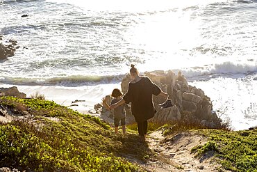 A teenage girl and her brother running down a path towards a sandy beach, Walker Bay Nature Reserve, South Africa