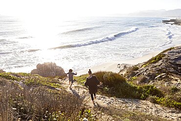 A teenage girl and her brother running down a path towards a sandy beach, Walker Bay Nature Reserve, South Africa