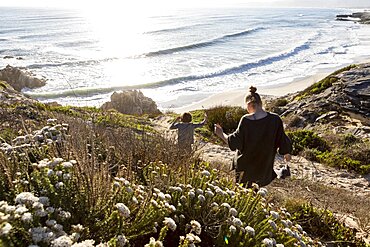 A teenage girl and her brother running down a path towards a sandy beach, Walker Bay Nature Reserve, South Africa