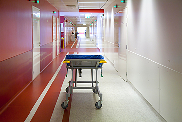 Corridor and waiting areas of a modern hospital with seating, a trolley bed with blue mattress