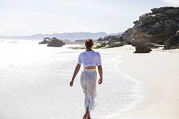 Teenage girl walking on a sandy beach at the water's edge