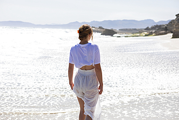 Teenage girl alone on a sandy beach in South Africa by the water's edge looking at the coastal view