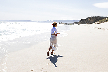 Teenage girl dancing alone on a sandy beach in South Africa by the water's edge
