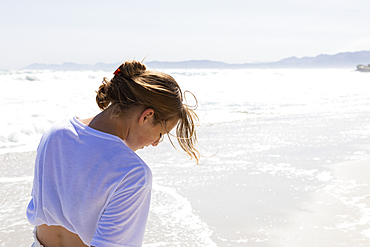 Teenage girl walking on a sandy beach at the water's edge