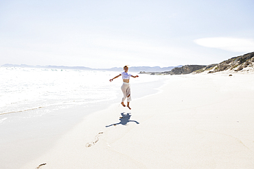 Teenage girl dancing alone on a sandy beach in South Africa by the water's edge