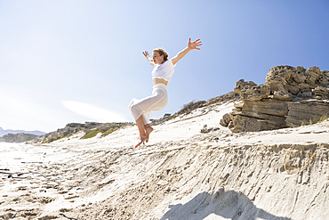 A teenage girl leaping from a sand dune into the soft sand below.