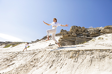 A teenage girl leaping from a sand dune into the soft sand below.