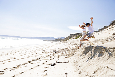 Two children leaping off sand dune on a beach