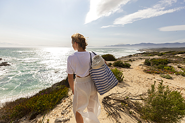 Teenage girl standing on top of a cliff looking over the coastline and inlet.