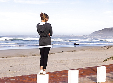 A teenage girl balancing on posts on a sandy beach, Grotto Beach, Western Cape, South Africa