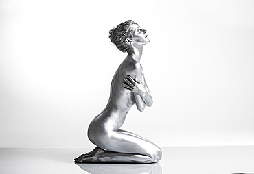 Nude Caucasian woman with silver body paint kneeling, side view, arms crossed across her body