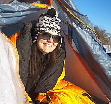 Woman looking out of tent flap smiling wearing winter hat, Kingston, Ontario, Canada