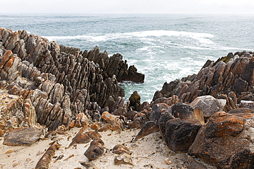 Jagged rocks and the rocky coastline of the Atlantic at De Kelders beach, waves breaking on shore, De Kelders, Western Cape, South Africa