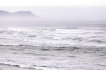 View over a sandy beach, mist rising and waves breaking on the Atlantic coastline, Voelklip Beach, Western Cape, South Africa