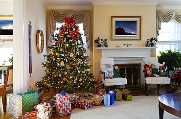 Living room with Christmas tree and gifts, traditional decorations, fireplace and furniture.