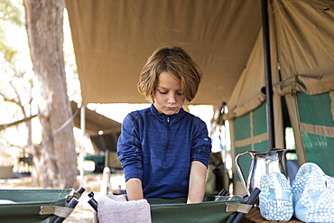 A boy preparing to wash his face in a canvas basin at a tented camp in the Okavango Delta, Okavango Delta, Botswana