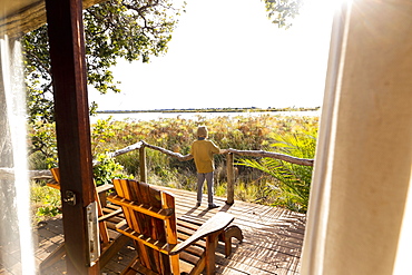 Young boy on wooden deck looking out over marshlands, Okavango Delta, Botswana