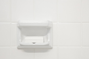 A white tiled wall of a bathroom or shower room, with a shaped porcelain recess. A block of soap.