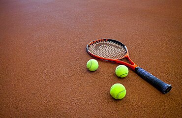 A hard tennis court and a tennis raquet,with three balls.