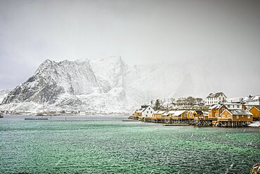 Sakrisoya Island, the mountain coastline and small town in the Lofoten islands archipelago, winter, sleet, snow and mist