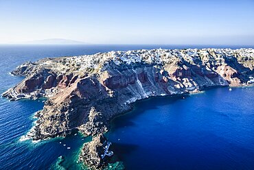 Aerial view of an island in the deep blue seas of the Aegean sea, rock formations, whitewashed houses perched on the cliffs.