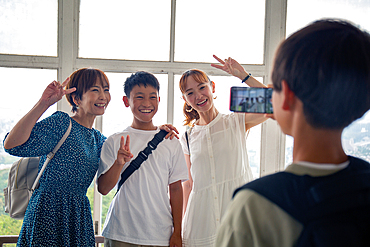 A boy using his mobile phone to take a picture of three Japanese people, a 13 year old boy, his mother and a friend.