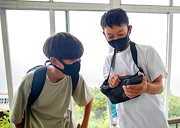 Two 13 year old Japanese boys in face masks, friends looking at a mobile phone screen.