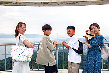 Four Japanese people on a outing, two mature women and two 13 year old boys, in a row, on a viewing platform.