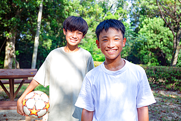 Two 13 year old boys in a park with a football in summer.