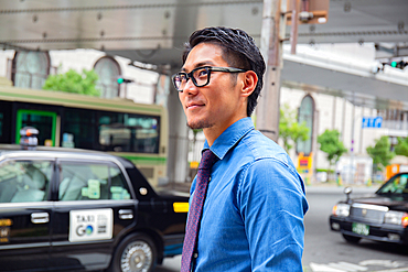 A young businessman in the city, on the move,  a man in a blue shirt and tie, a taxi behind him.