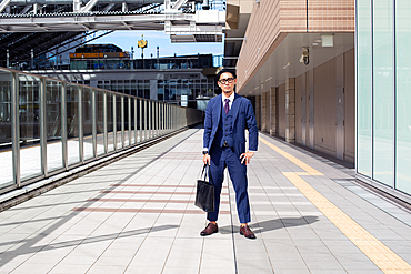 A young businessman in the city, on the move, a man in a suit with a laptop bag, standing legs apart on a walkway.