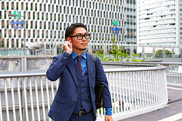 A young businessman in a blue jacket, shirt and tie, standing on a downtown walkway.