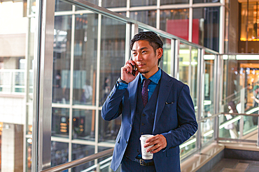 A young businessman in a blue suit on the move in a city downtown area, speaking on his mobile phone.