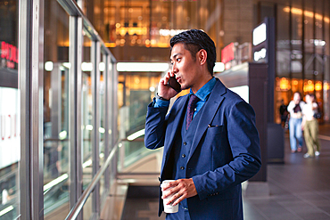 A young businessman in a blue suit on the move in a city downtown area, speaking on his mobile phone.