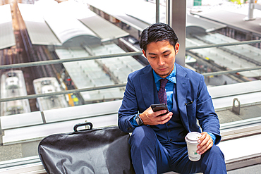 A young businessman in a blue suit in a city, looking at his mobile phone screen, texting or reading a message.