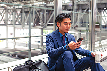 A young businessman in a blue suit in a city, looking at his mobile phone screen, texting or reading a message.