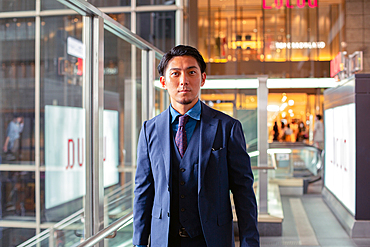 A young businessman in a blue suit on the move in a city downtown area, front view.