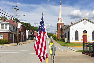 American flag flying on a quiet main street with houses and a church.